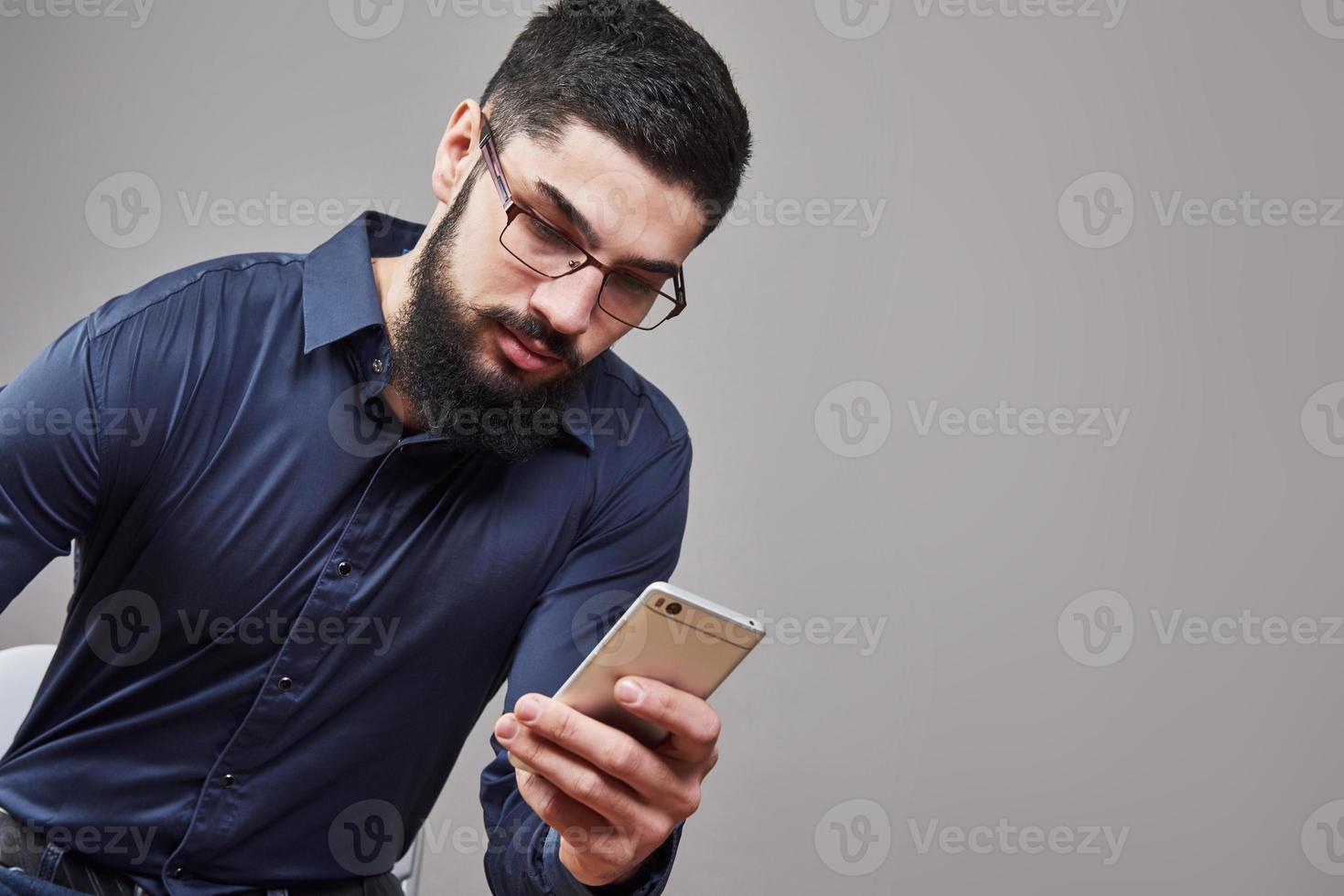 glücklicher Mann mit Brille, der SMS auf grauem Hintergrund schreibt foto