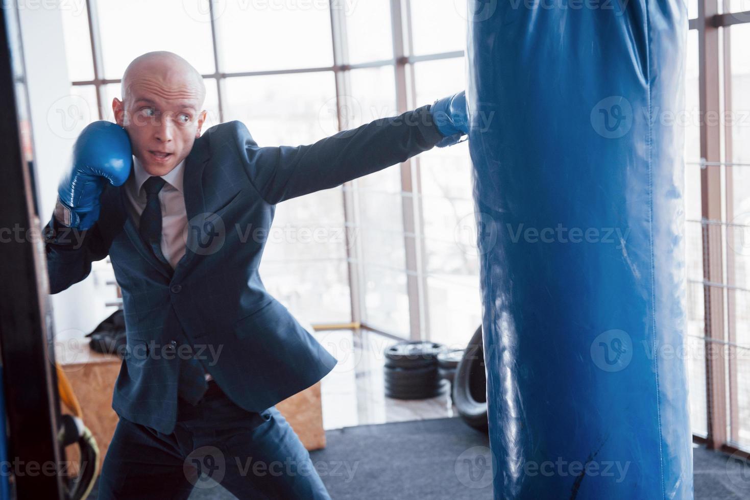 ein wütender kahlköpfiger geschäftsmann schlägt im fitnessstudio eine boxbirne. Konzept der Wutbewältigung foto