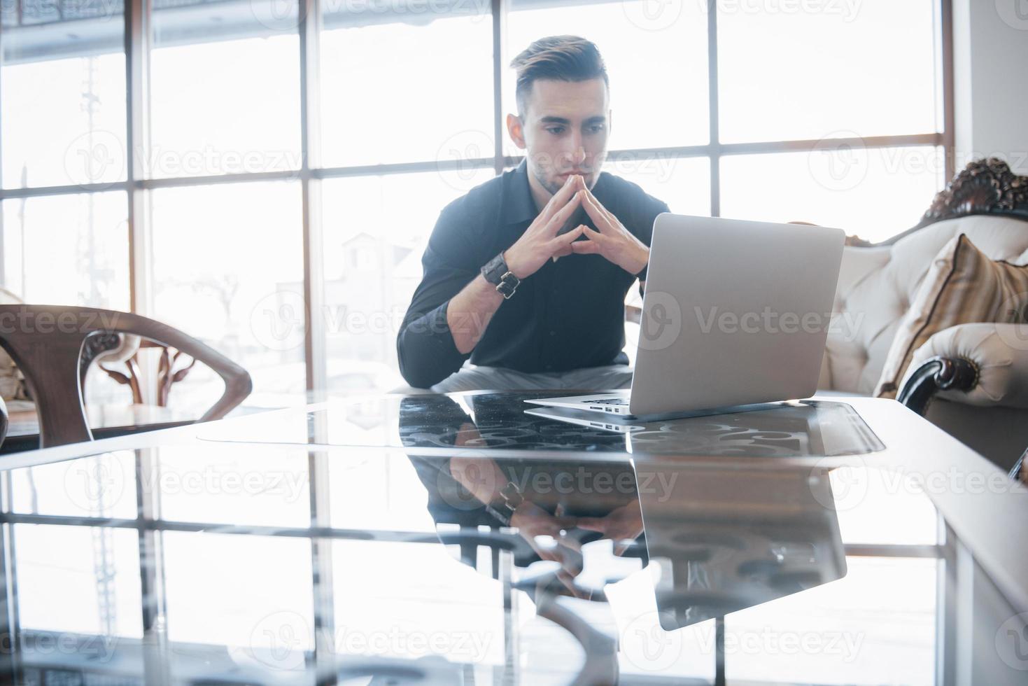junger Geschäftsmann, der an einem modernen Loft-Büro arbeitet. Mann, der weißes Hemd trägt und zeitgenössischen Laptop verwendet. Panoramafenster Hintergrund foto
