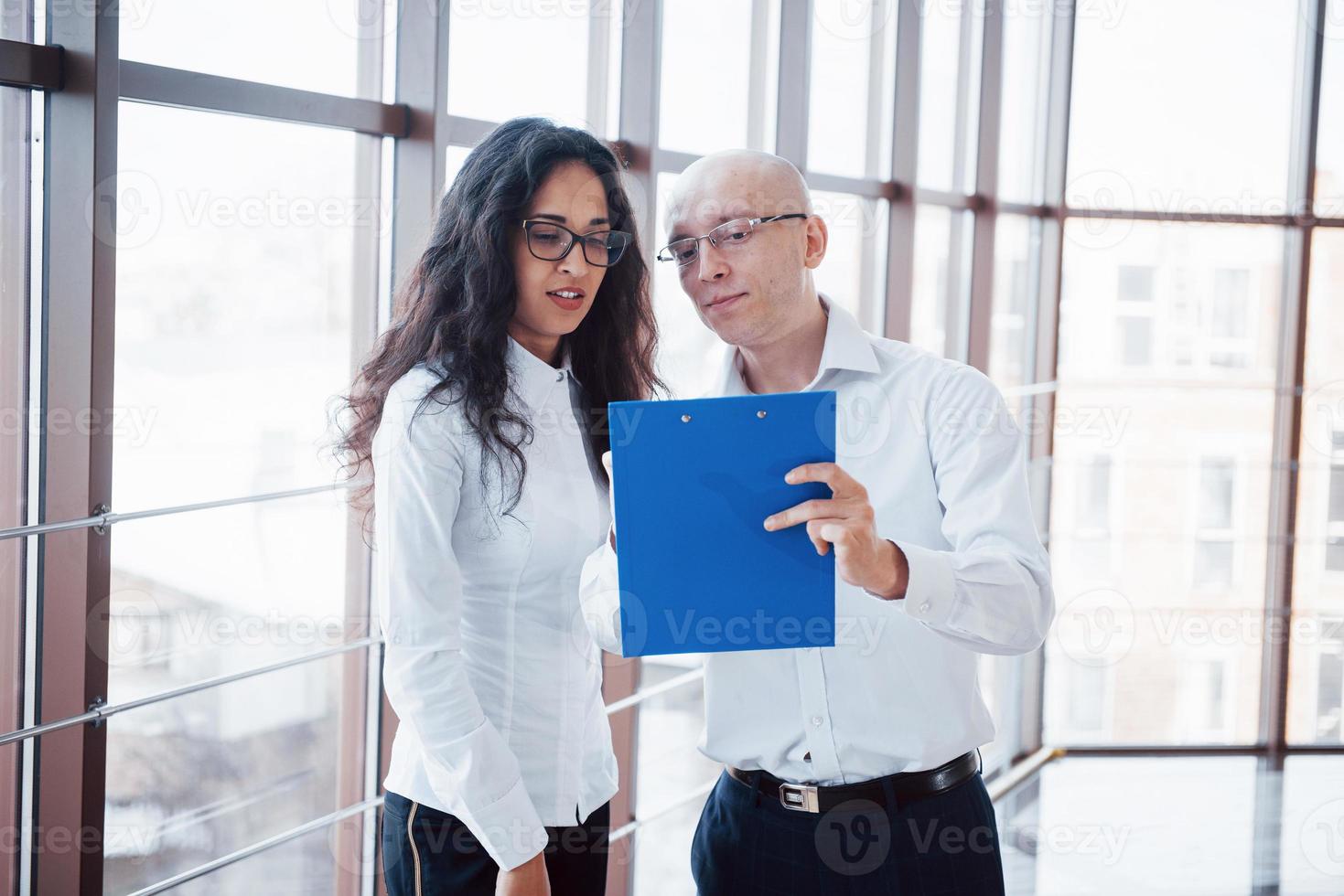 Geschäftsmann und Geschäftsfrau, die ein Diagramm auf den Platten- und Papierdokumenten am Fenster auf dem Hintergrund des Stadtbüros auf einem hohen Stockwerk studieren foto