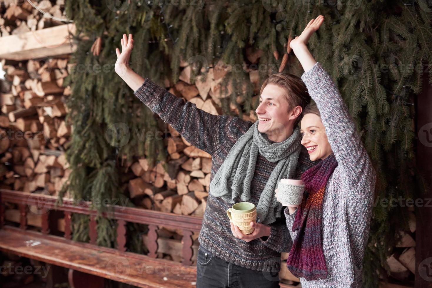 Foto von glücklichem Mann und hübscher Frau mit Tassen im Freien im Winter. Winterurlaub und Urlaub. Weihnachtspaare des glücklichen Mannes und der Frau trinken heißen Kaffee. Hallo Nachbarn