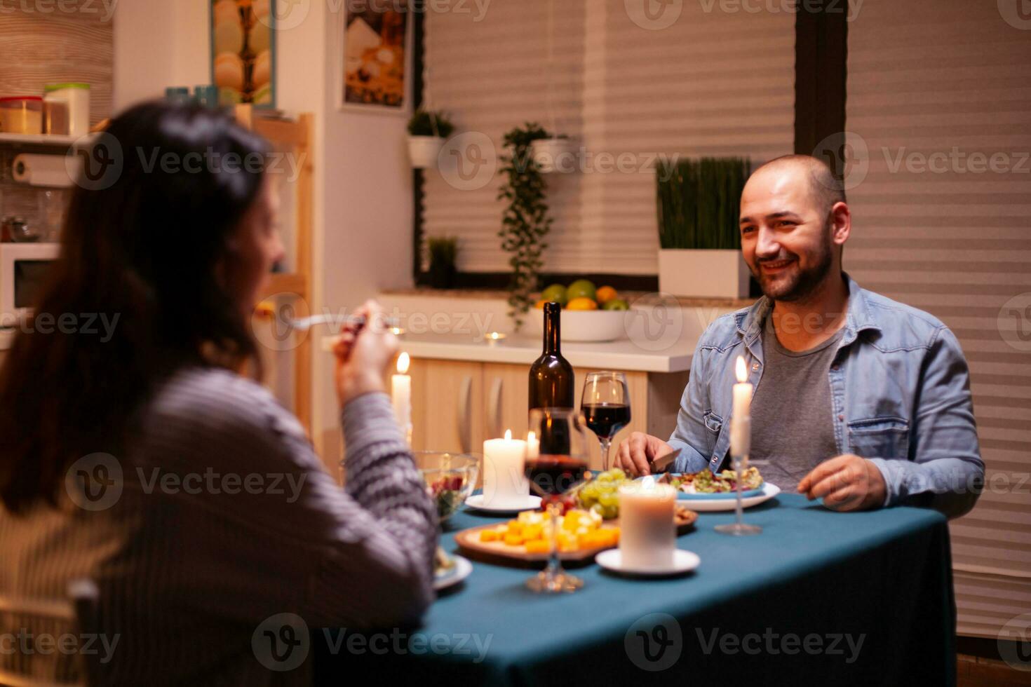 romantisch Abendessen mit Mann im Vordergrund Gefühl glücklich mit Ehefrau im Essen Zimmer. entspannen glücklich Menschen klirren, Sitzung beim Tabelle im Küche, genießen das Mahlzeit, feiern Jubiläum. foto