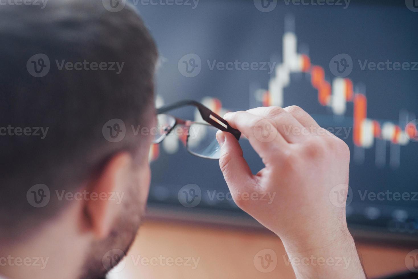 Daten analysieren. Nahaufnahme eines jungen Geschäftsmannes, der eine Brille hält und die gff anschaut, während er in einem Kreativbüro arbeitet foto
