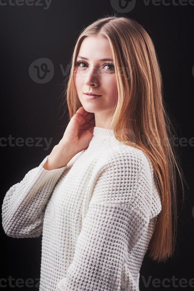 Nahaufnahme Porträt einer schönen jungen Frau in weißem Pullover und Jeans, isoliert auf schwarzem Hintergrund foto