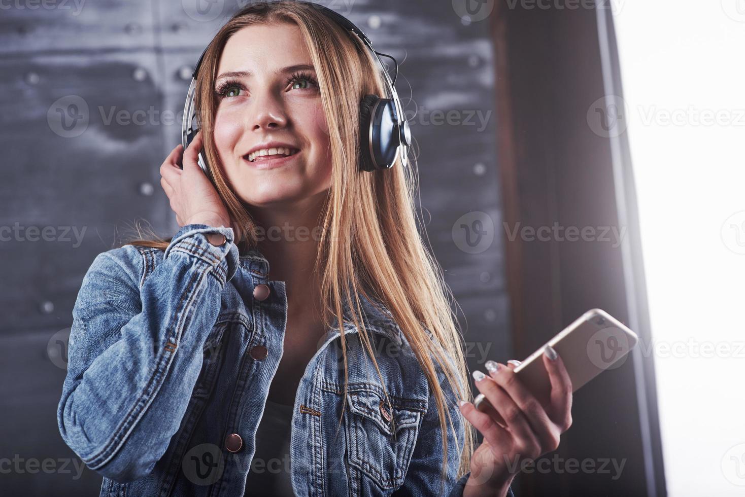 Mode, Kleidung, Menschenkonzept. Nahaufnahme attraktive sexy junge Frau mit Jeansjacke. Mädchen posiert im Studio hört Musik über Kopfhörer foto