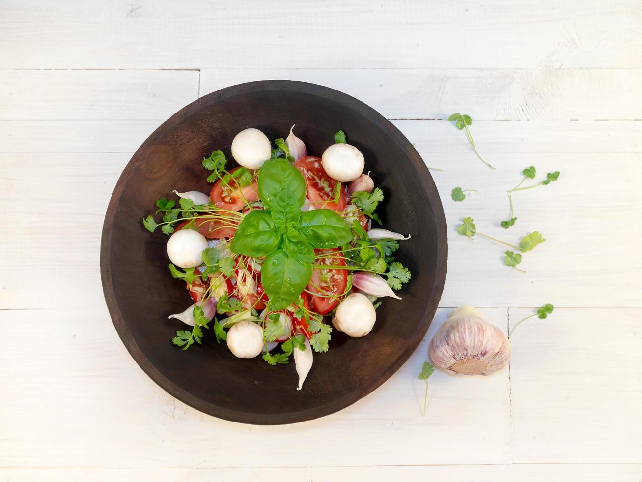 Salat mit Basilikum und Champignons in einem dunklen Teller, in der Nähe ist Knoblauch foto