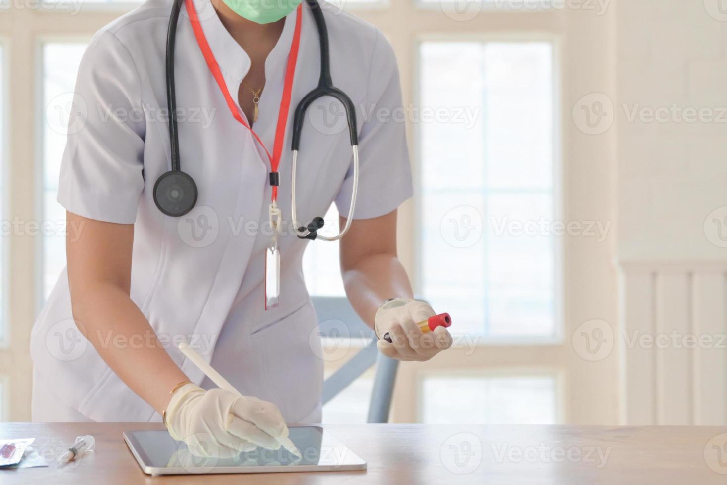 Abgeschnittene Aufnahme einer Krankenschwester, die medizinische Handschuhe trägt, die auf dem Tablet-Bildschirm schreibt und die Blutröhrchen greift, um Daten zu speichern. foto