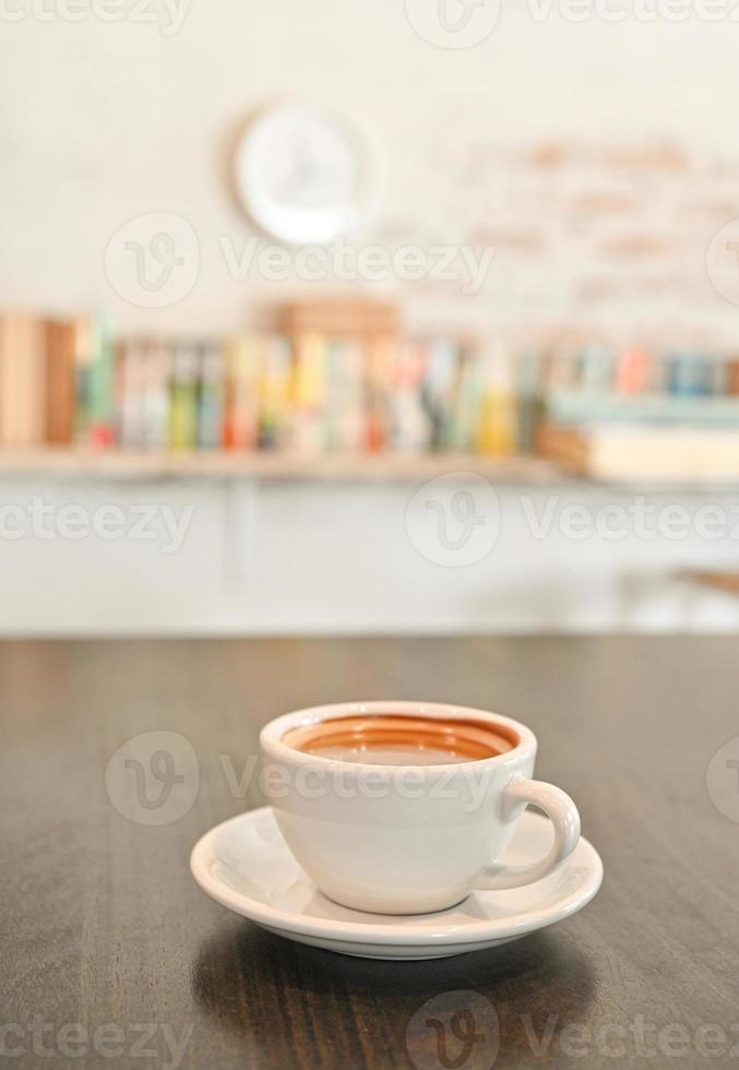 weiße Kaffeetasse auf Holztisch, Hintergrund, Bücherregal. foto