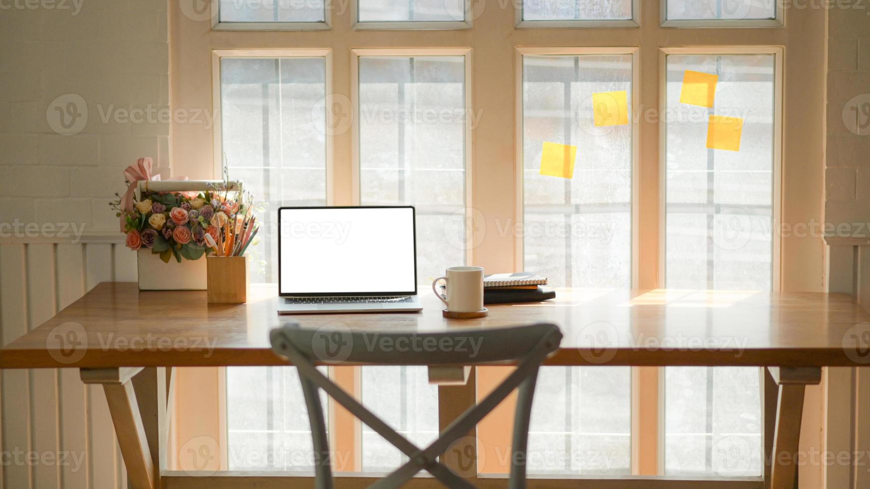 Ausgeschnittene Aufnahme eines klassischen Arbeitsplatzes mit Laptop, Kaffeetasse und Schreibwaren auf einem Holztisch in der Nähe des Fensters. foto