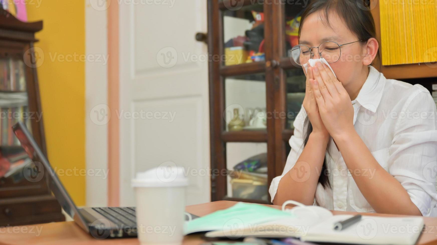 asiatische frau benutzt ein taschentuch, um ihr gesicht zu bedecken und zu niesen. Sie arbeitet zu Hause, um sich vor dem Coronavirus oder Covid-19 zu schützen. foto