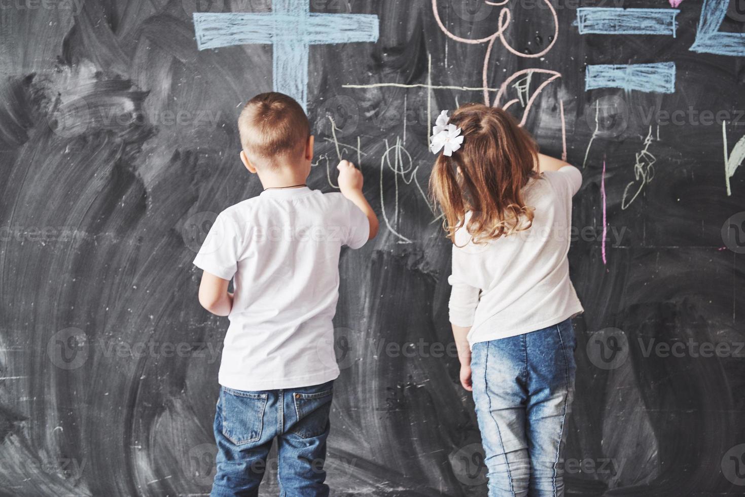süße kleine Mädchen und Jungen zeichnen mit Buntstiftfarbe an der Wand. Werke des Kindes. süße Schülerin schreibt auf Tafel foto
