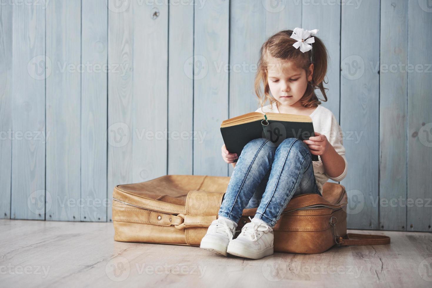 bereit für große Reisen. glückliches kleines Mädchen, das ein interessantes Buch liest, das eine große Aktentasche trägt und lächelt. Reise-, Freiheits- und Vorstellungskonzept foto