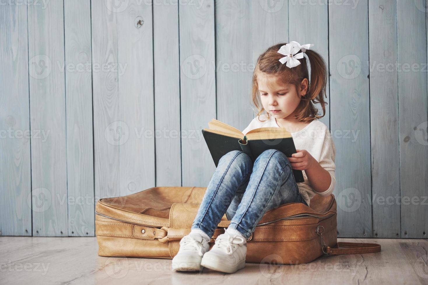 bereit für große Reisen. glückliches kleines Mädchen, das ein interessantes Buch liest, das eine große Aktentasche trägt und lächelt. Reise-, Freiheits- und Vorstellungskonzept foto