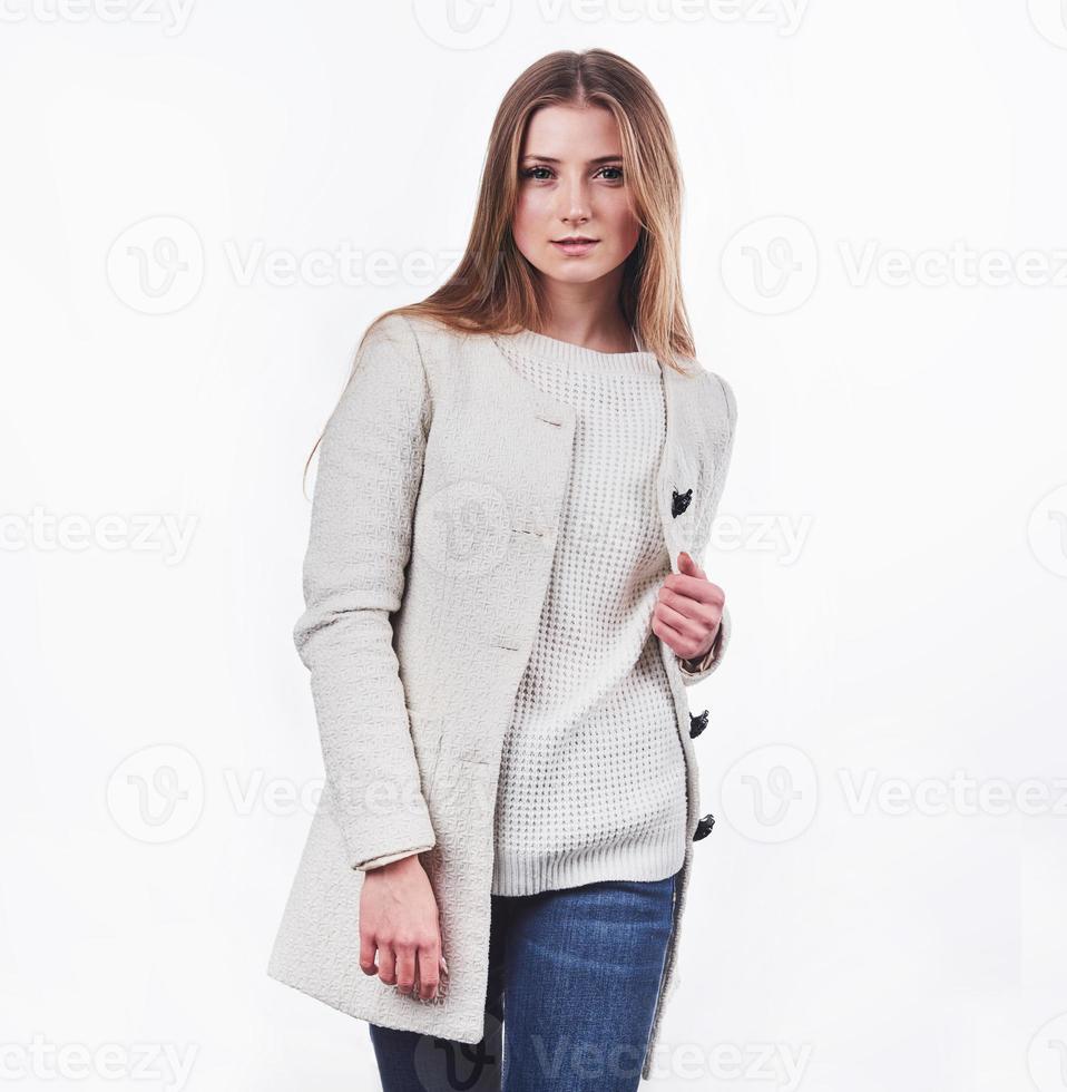 lächelnde blonde Frau in stylischer Strickjacke posiert in Wollpullover posiert gegen eine weiße Wand foto