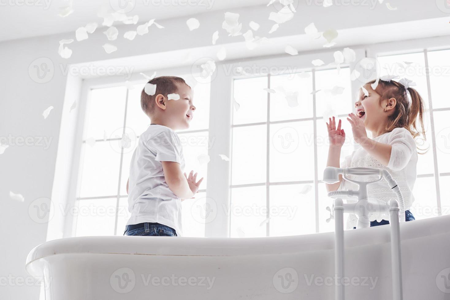 Kind spielt mit Rosenblättern im Badezimmer zu Hause. kleines mädchen und junge fawing spaß und freude zusammen. das Konzept der Kindheit und die Verwirklichung von Träumen, Fantasie, Vorstellungskraft foto