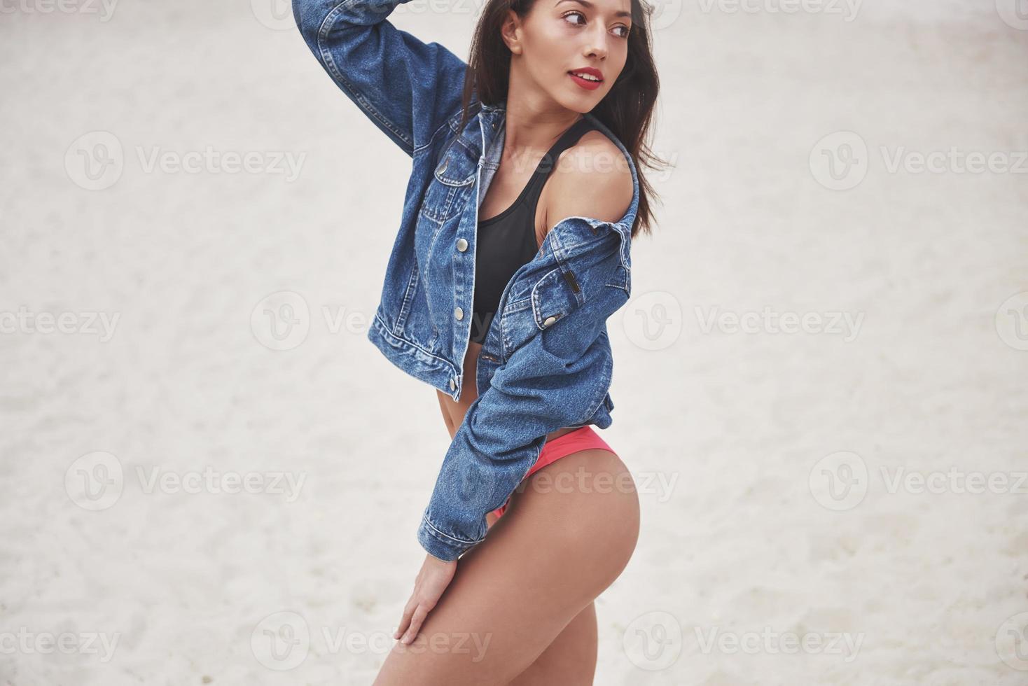 Schönes schlankes Luxusmädchen in Bikini und Jeansjacke am Sandstrand auf einer tropischen Insel. sexy gebräunter Körper und perfekte Figur foto