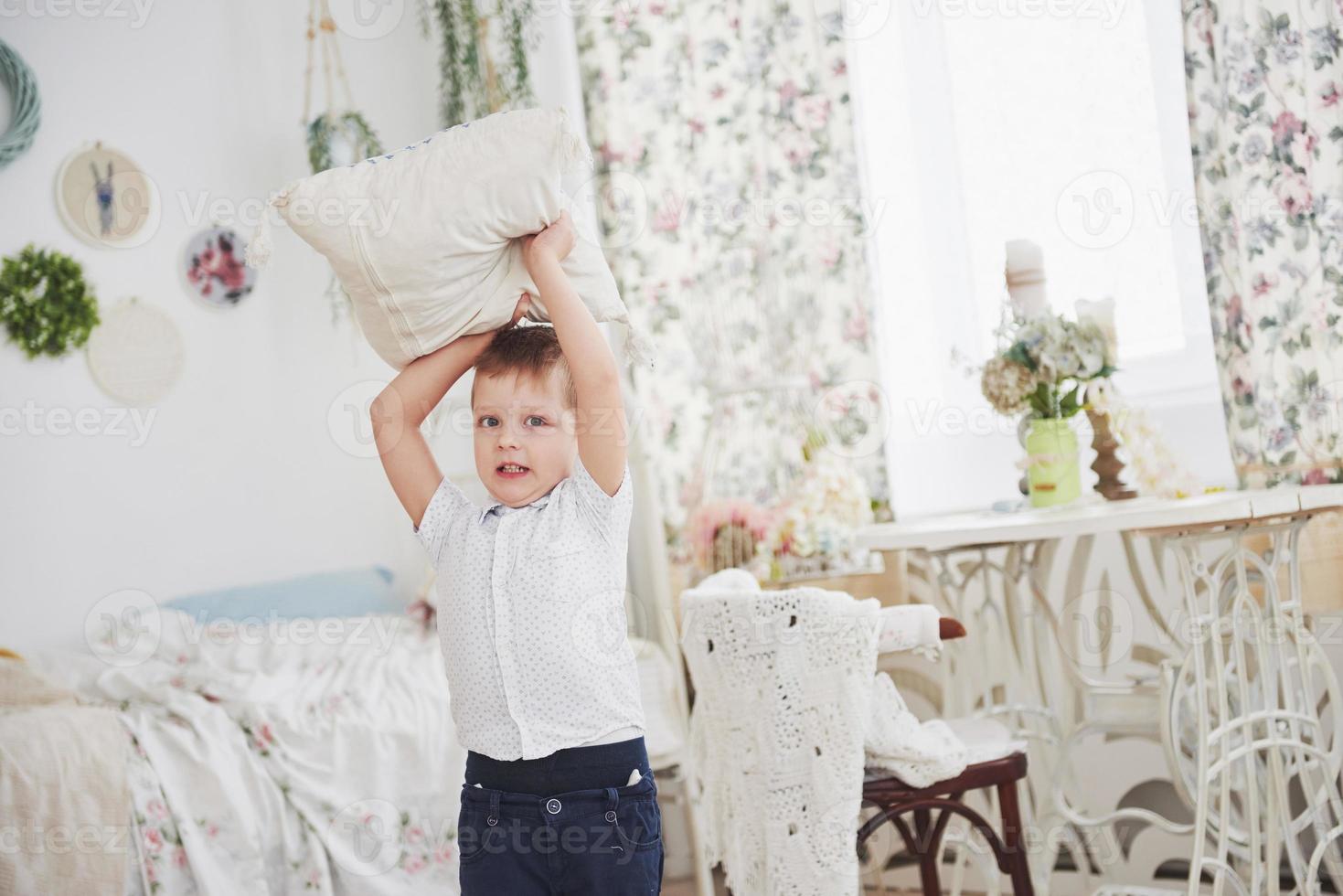 kleiner Junge im weißen Hemd mit Kissen. Kissenschlacht foto