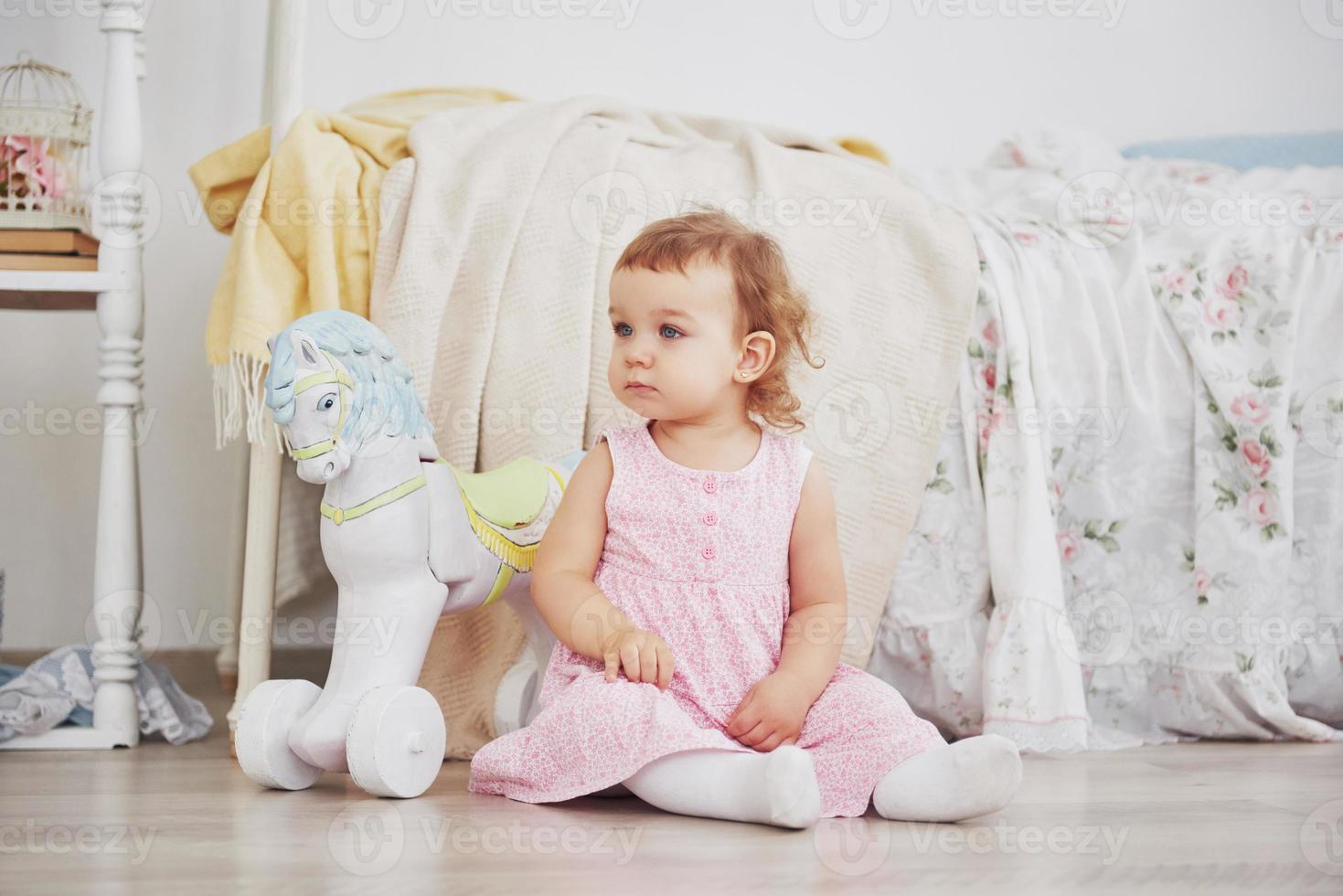 schönes kleines Mädchen, das Spielzeug spielt. blauäugige Blondine. weißer Stuhl. Kinderzimmer. glückliches kleines Mädchenporträt. Kindheit Konzept foto