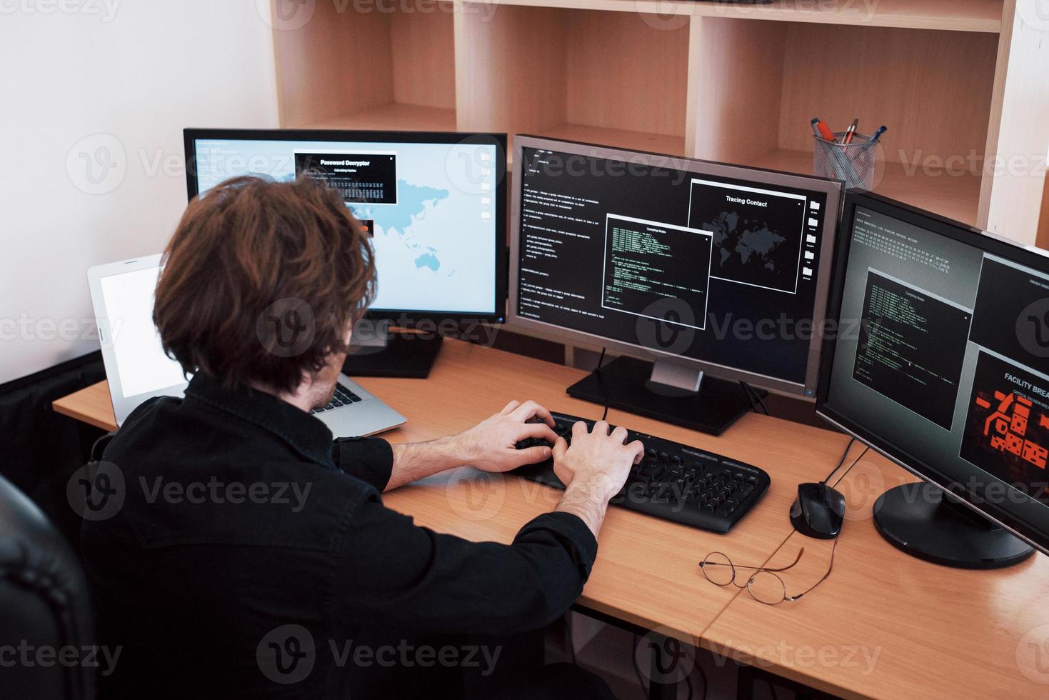 Der junge gefährliche Hacker bricht staatliche Dienste zusammen, indem er sensible Daten herunterlädt und Viren aktiviert. ein Mann benutzt einen Laptop mit vielen Monitoren foto