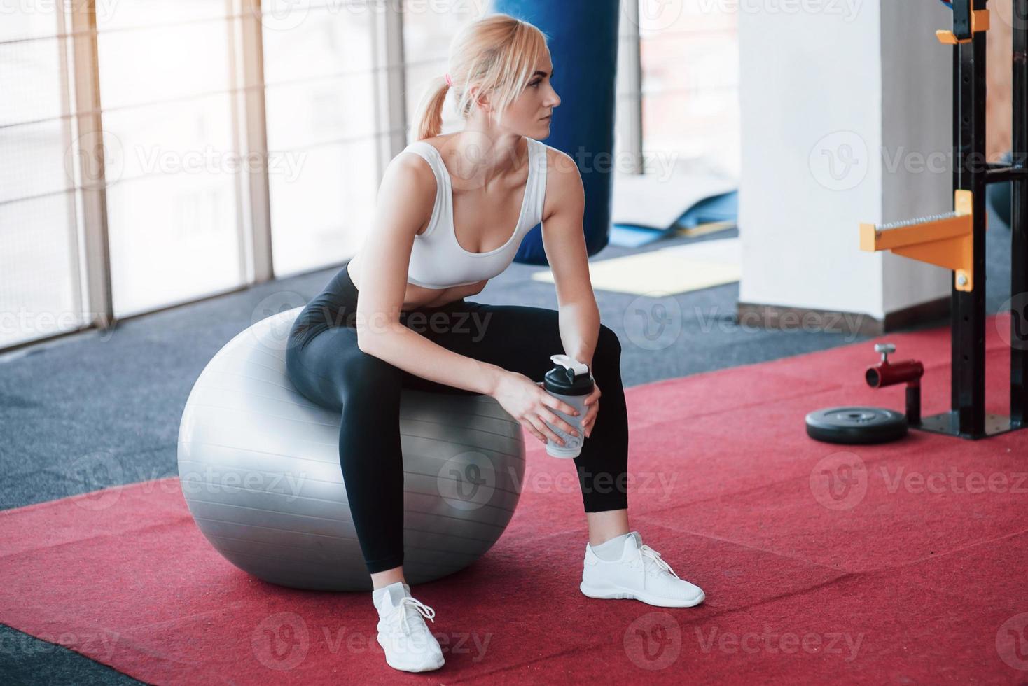 Entspannung nach dem Training. Blick auf eine schöne junge Frau, die wegschaut, während sie auf einer Trainingsmatte im Fitnessstudio sitzt foto