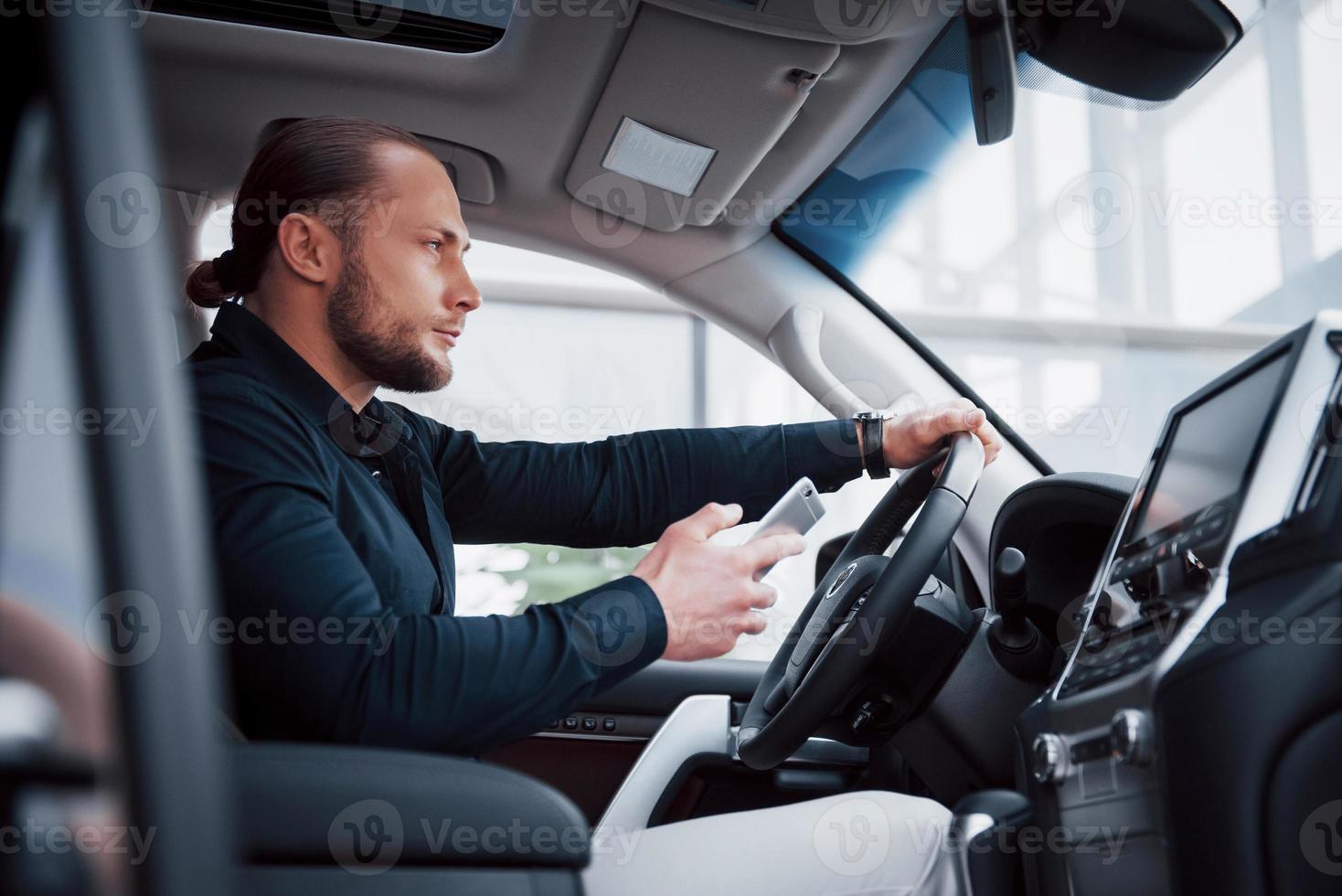 Zufriedener junger Geschäftsmann, der beim Autofahren auf das Handy schaut foto