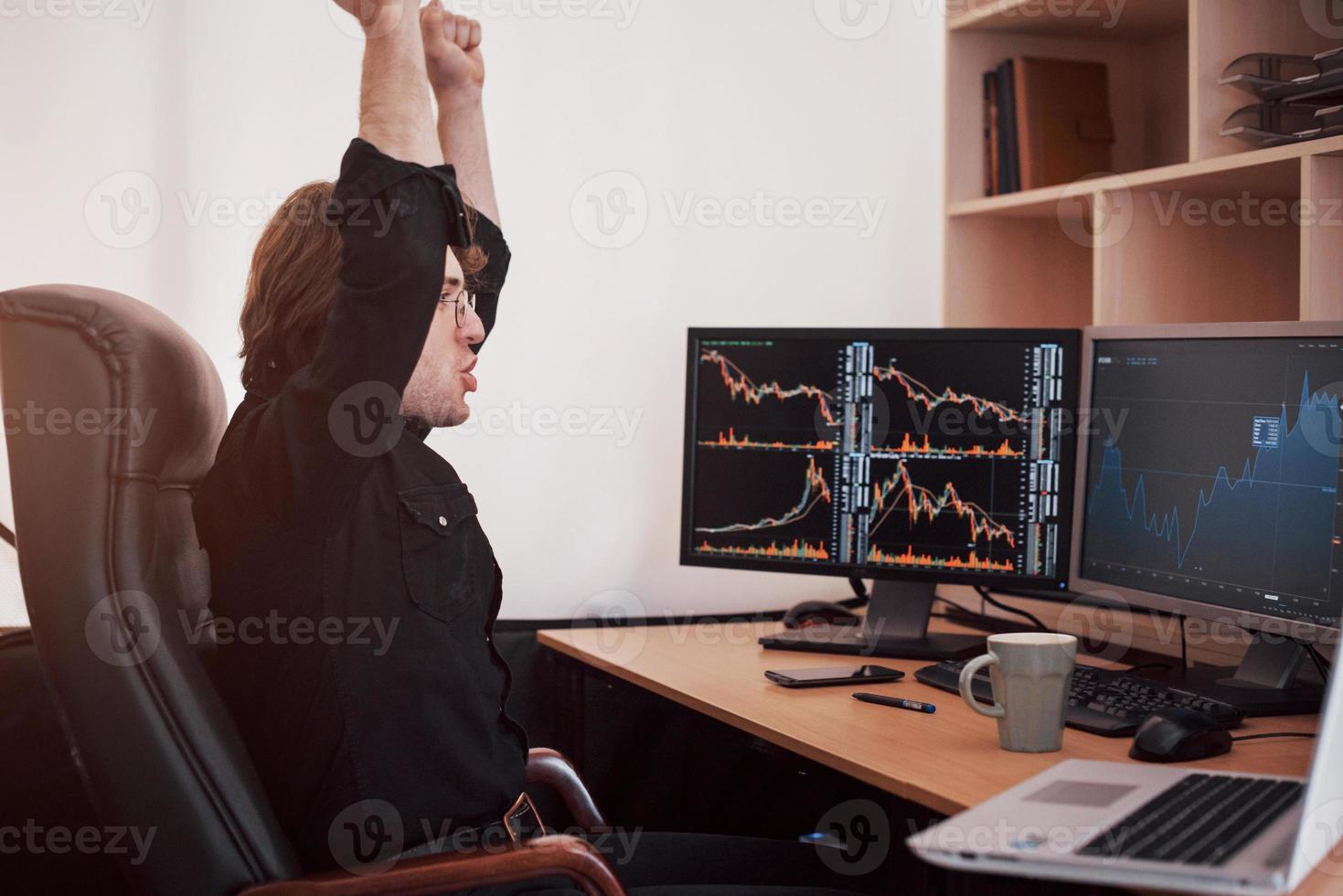 junger Börsenhändler-Broker, der sich am Arbeitsplatz die Hände ausstreckt, er hat zum ersten Mal große Erfolge an der Börse erzielt foto