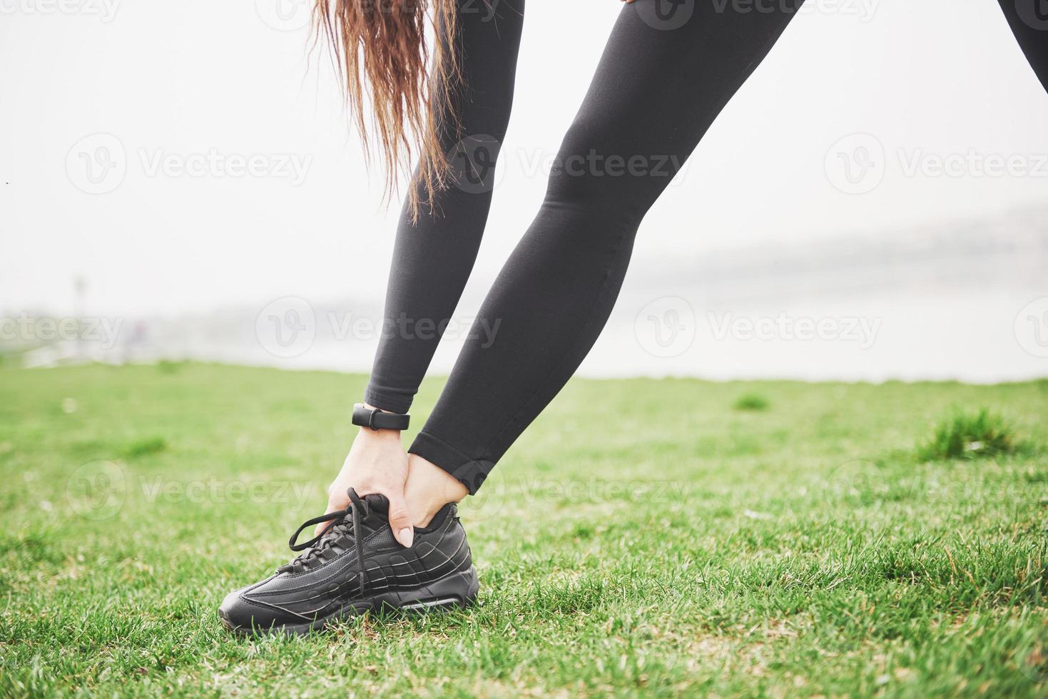 junge Fitnessfrau, die Beine ausdehnt, bevor sie im Park läuft foto