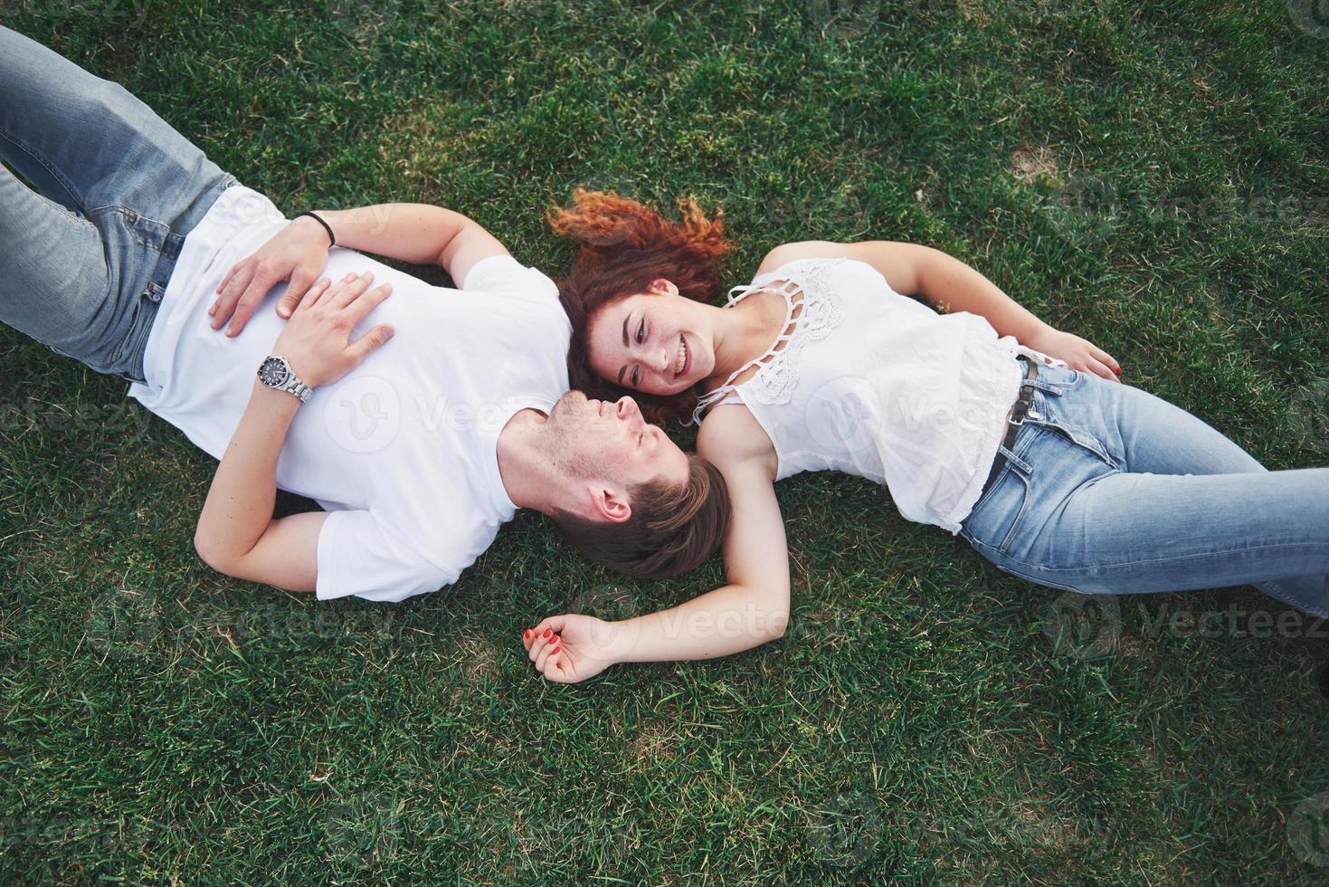 Romantisches Paar junger Leute, die auf Gras im Park liegen. Sie sehen glücklich aus. Sicht von oben. foto