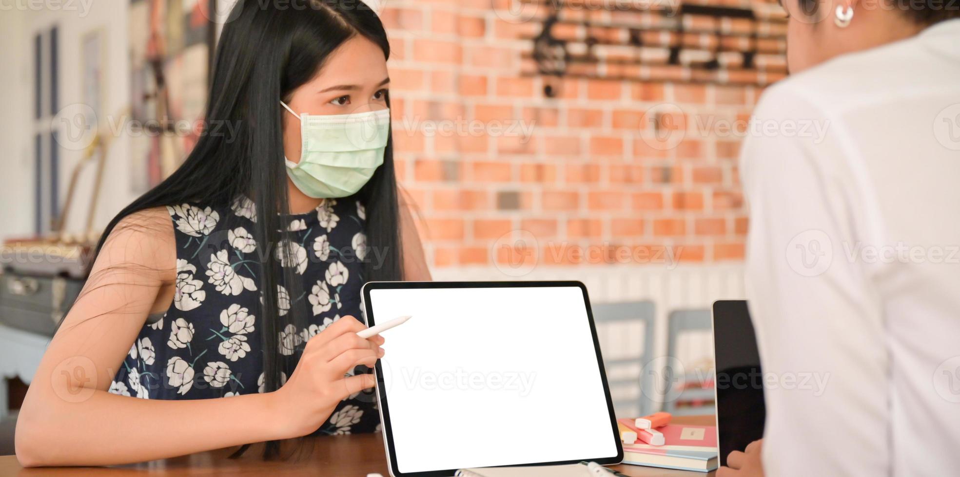 Eine Versicherungsvertreterin, die eine Maske trägt, führt mit einem Tablet ein Coronavirus-Gesundheitspaket ein. foto
