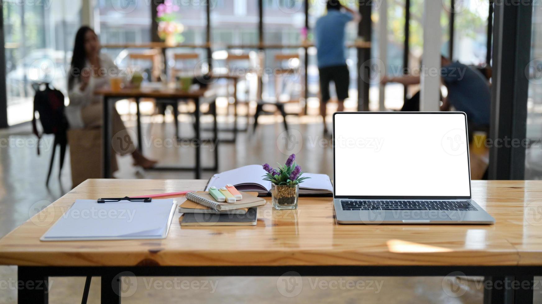 Ausgeschnittene Aufnahme von Laptop, Notizen und Büromaterial auf einem Holzschreibtisch in einem komfortablen gemeinsamen Arbeitsbereich. foto