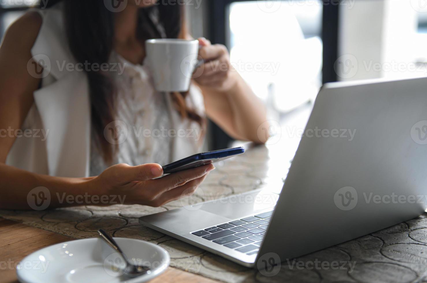 weibliche Geschäftsleute essen Kaffee und benutzen Smartphone. sie arbeitet zwischen Kaffeebremse, Laptop auf dem Schreibtisch. foto