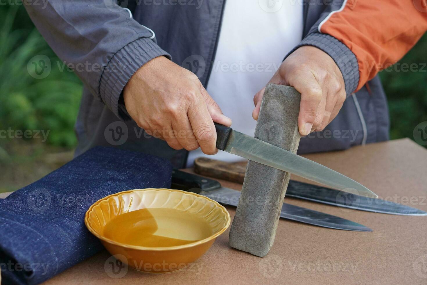 Nahaufnahme Mannhände schärfen Messer auf Wetzsteinschärfer oder Schleifstein. Konzept, Wartungswerkzeuge zum Kochen, Messer scharf machen, nicht stumpf für lange Lebensdauer. origineller Stil. foto