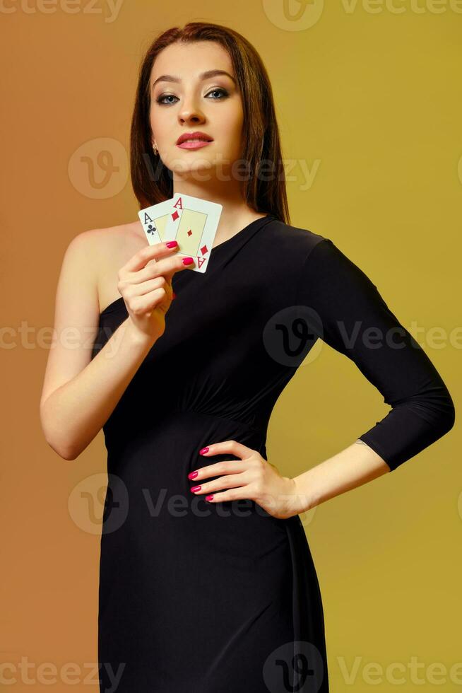 blond Mädchen mit hell bilden, im schwarz Kleid ist zeigen zwei Asse, posieren gegen bunt Hintergrund. Glücksspiel, Poker, Kasino. Nahansicht. foto