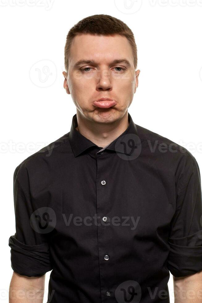 gut aussehend jung Mann im ein schwarz Hemd ist Herstellung Gesichter, während Stehen isoliert auf ein Weiß Hintergrund foto