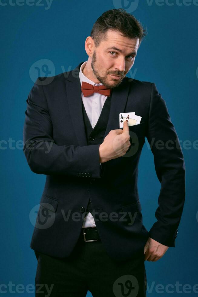 Mann im schwarz klassisch passen und rot Krawatte zeigen zwei spielen Karten während posieren gegen Blau Studio Hintergrund. Glücksspiel, Poker, Kasino. Nahansicht. foto