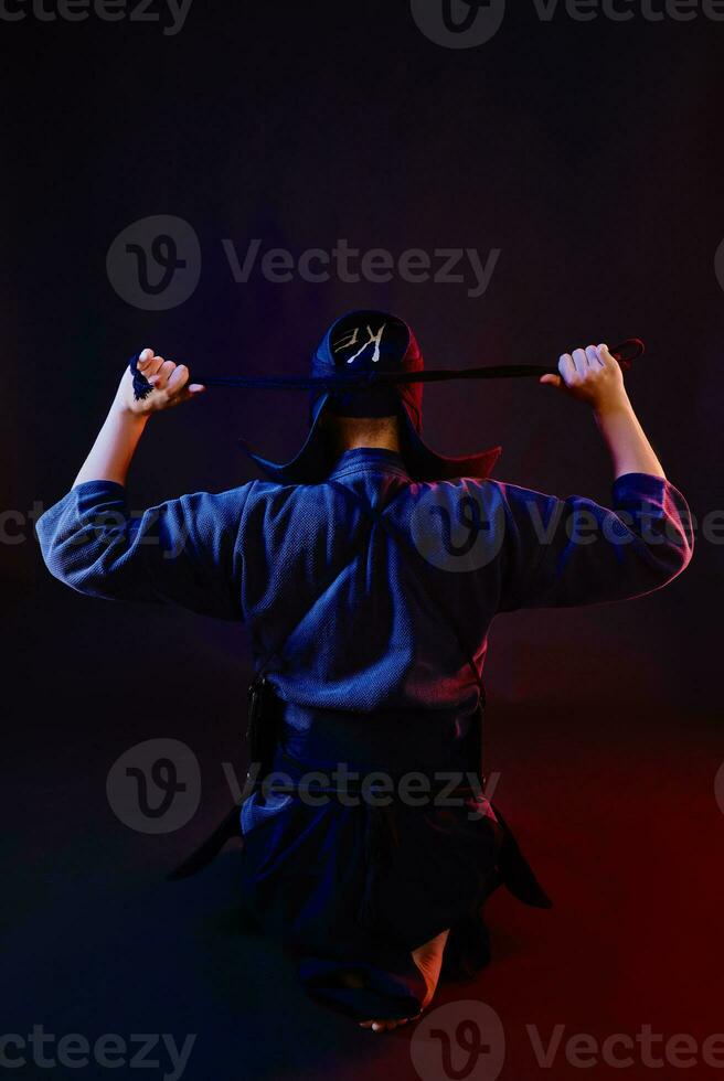 schließen oben Schuss, Kendo Kämpfer tragen im ein Rüstung und traditionell Kimono ist binden das Schnürung auf seine Helm Stehen zurück gegen ein schwarz Hintergrund. foto