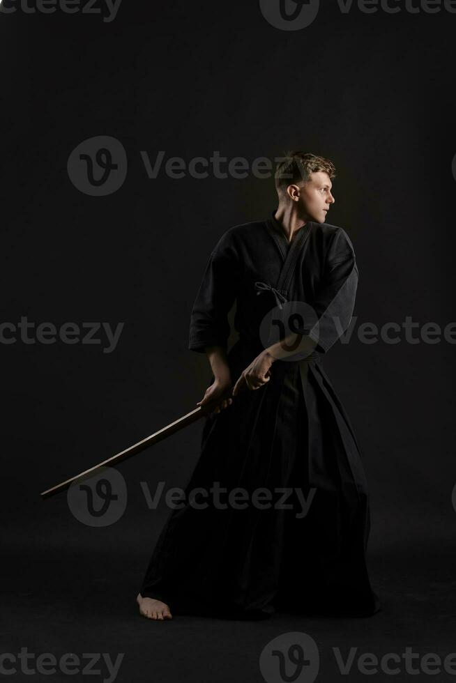 Kendo Guru tragen im ein traditionell japanisch Kimono ist üben kriegerisch Kunst mit das shinai Bambus Schwert gegen ein schwarz Studio Hintergrund. foto