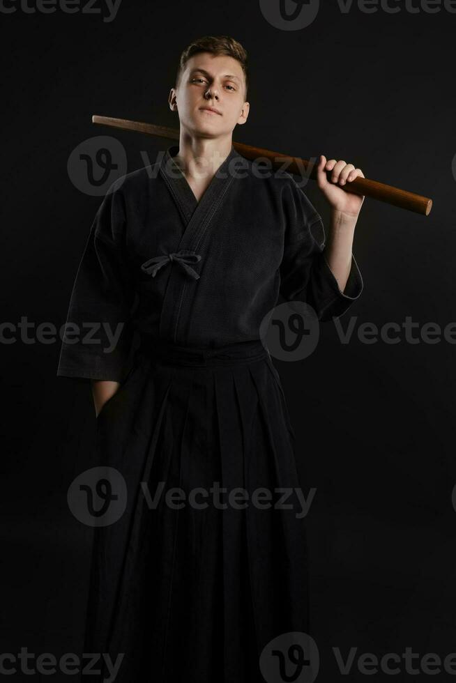 Kendo Guru tragen im ein traditionell japanisch Kimono ist üben kriegerisch Kunst mit das shinai Bambus Schwert gegen ein schwarz Studio Hintergrund. foto