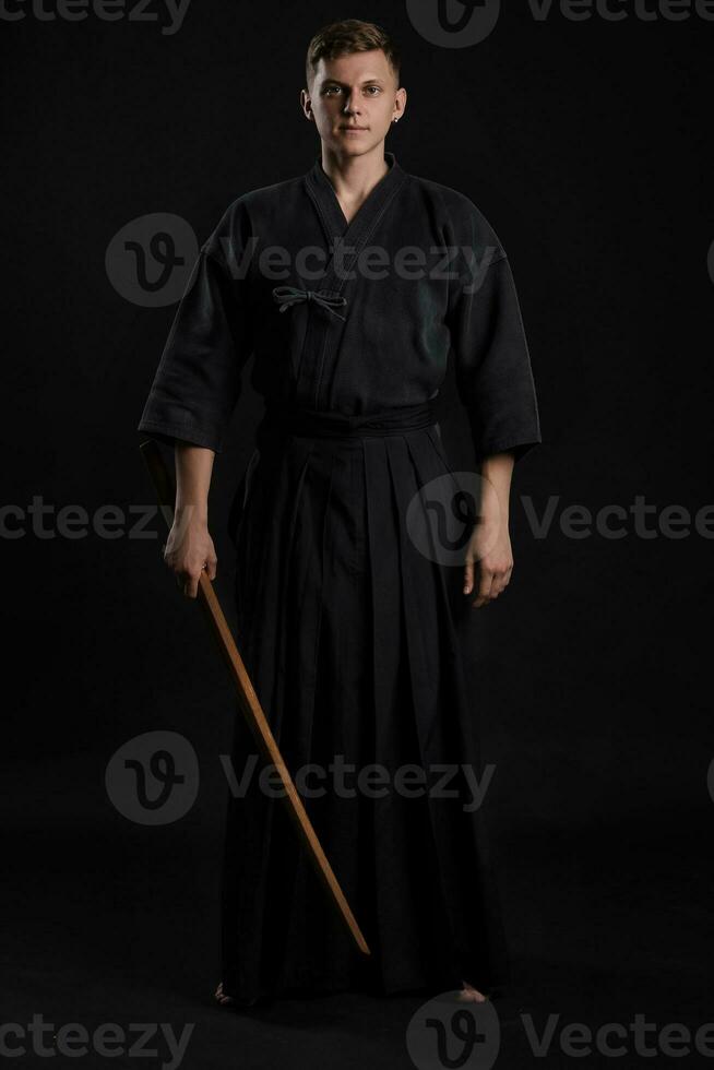 Kendo Guru tragen im ein traditionell japanisch Kimono ist üben kriegerisch Kunst mit das shinai Bambus Schwert gegen ein schwarz Studio Hintergrund. foto