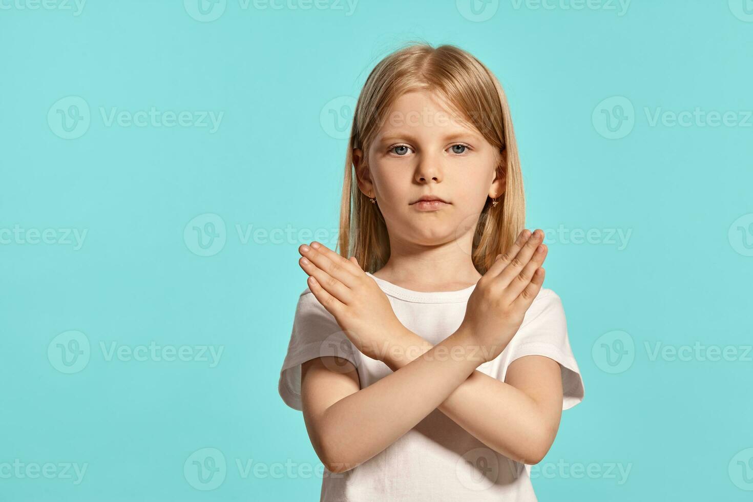 Nahansicht Studio Schuss von ein schön blond wenig Mädchen im ein Weiß T-Shirt posieren gegen ein Blau Hintergrund. foto