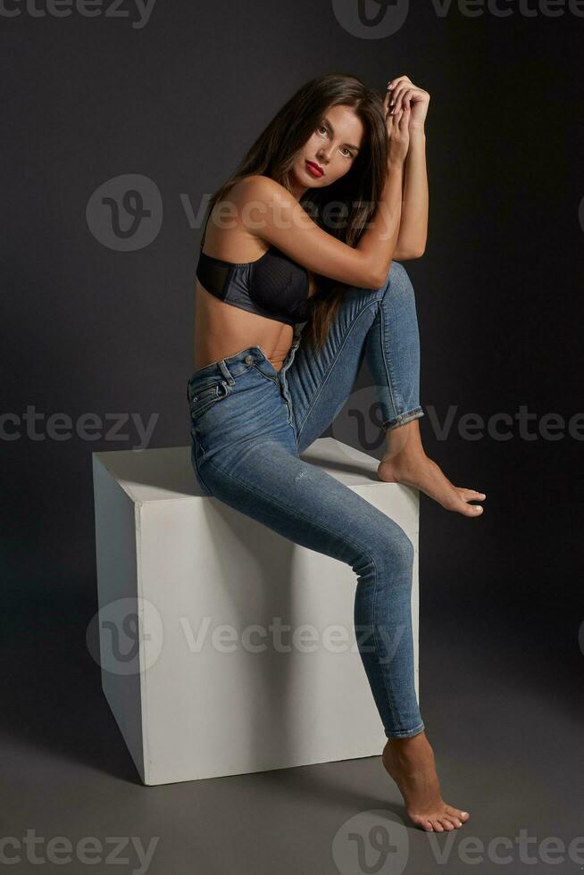 schön sexy Brünette Frau posieren im Studio, Sitzung, suchen beim Kamera. Mädchen tragen modisch Jeans und sinnlich Unterwäsche. foto