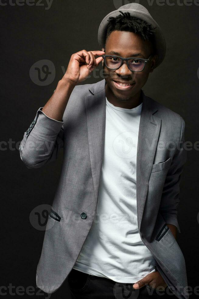 Nahansicht Porträt von gut aussehend schwarz Mann mit charmant lächeln. Studio Schuss von gut angezogen afrikanisch Kerl trägt Hut und Jacke. foto