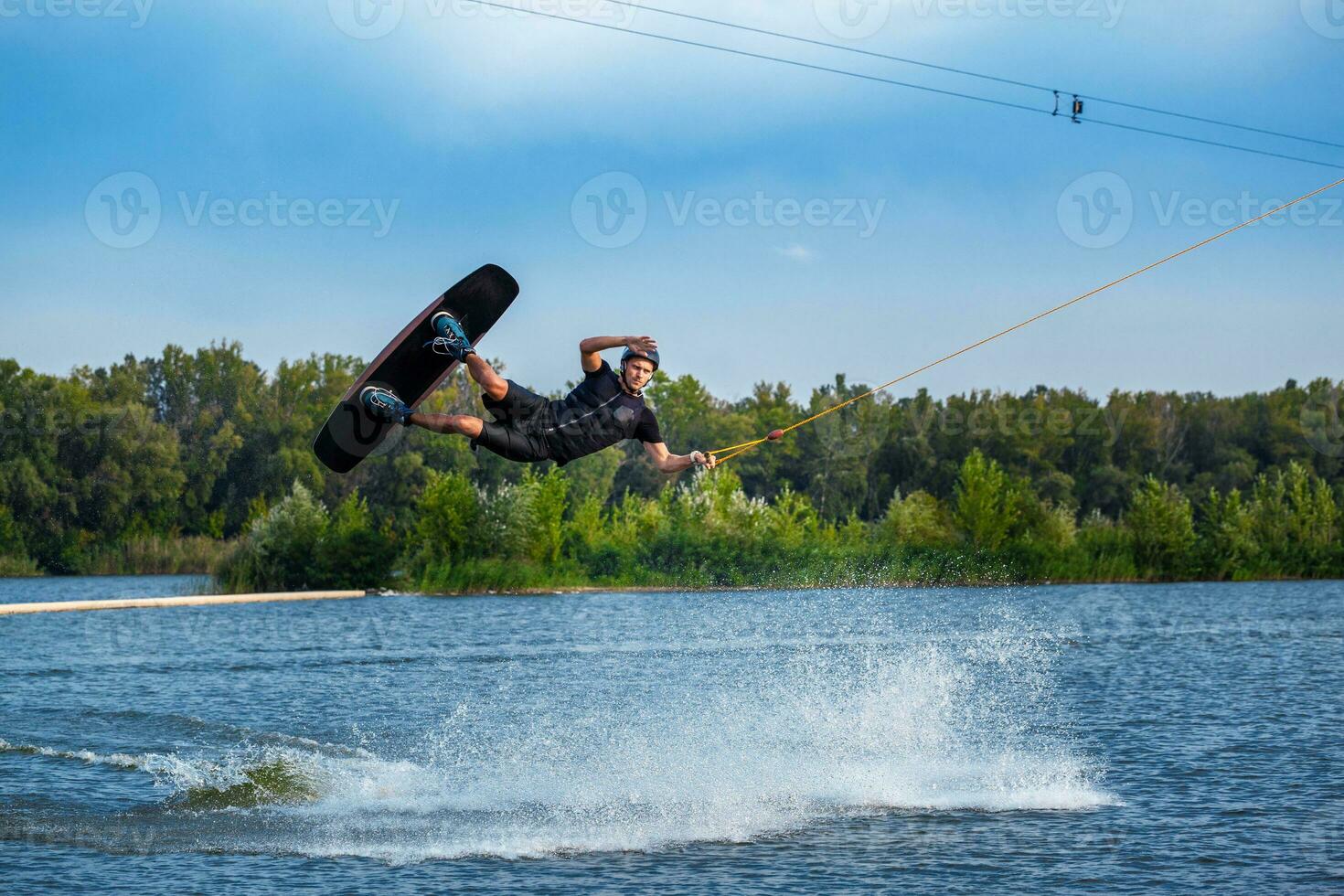 konzentriert Wakeboarder Springen mit Tafel Über Ruhe See Wasser Oberfläche Erstellen spritzt foto