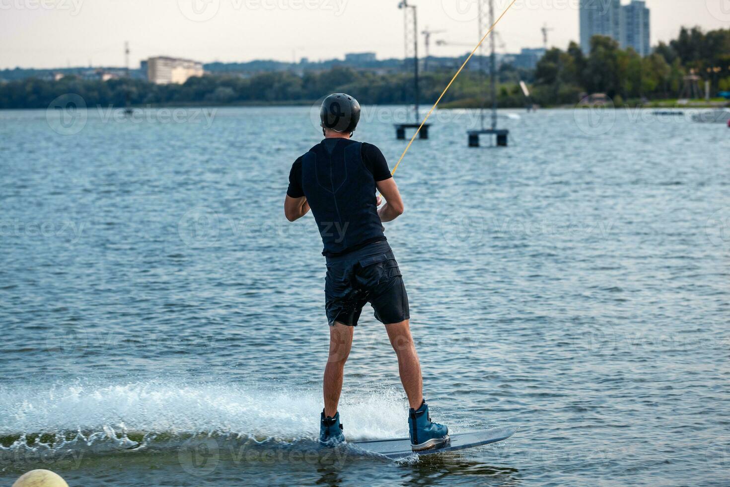 zurück Aussicht von sportlich Mann balancieren auf Wakeboard, Reiten auf Stadt Fluss foto