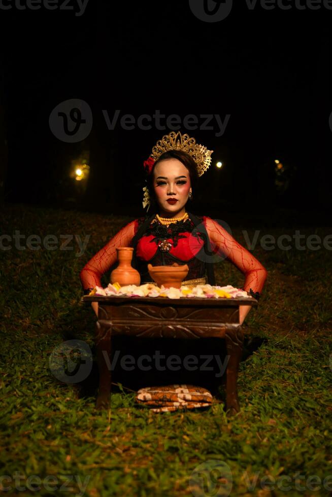 breit Schuss von ein asiatisch Mädchen im traditionell Kleider Sitzung im ein Wald mit ein Tabelle voll von Blumen foto