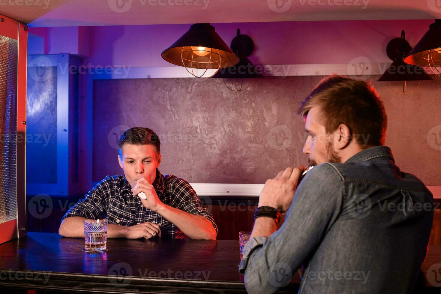 zwei jung Männer Rauch elektronisch Zigaretten im ein vapebar foto