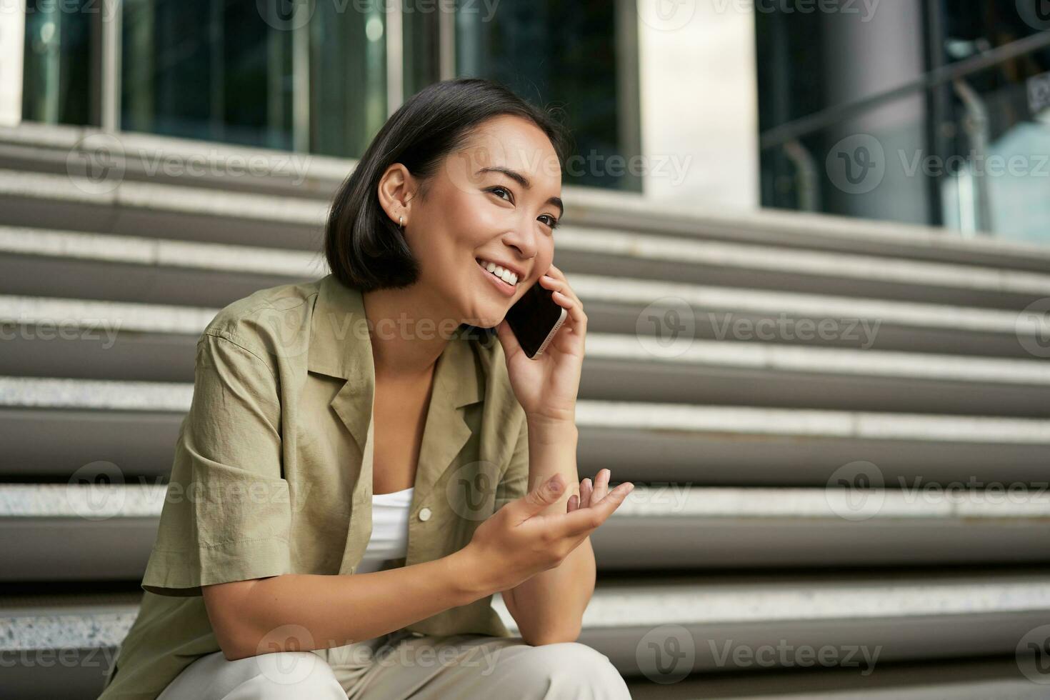 Porträt von schön asiatisch Mädchen Gespräche auf Handy, Mobiltelefon Telefon, sitzt auf Straße Stufen. Frau mit Smartphone lächelnd, Herstellung ein Anruf foto