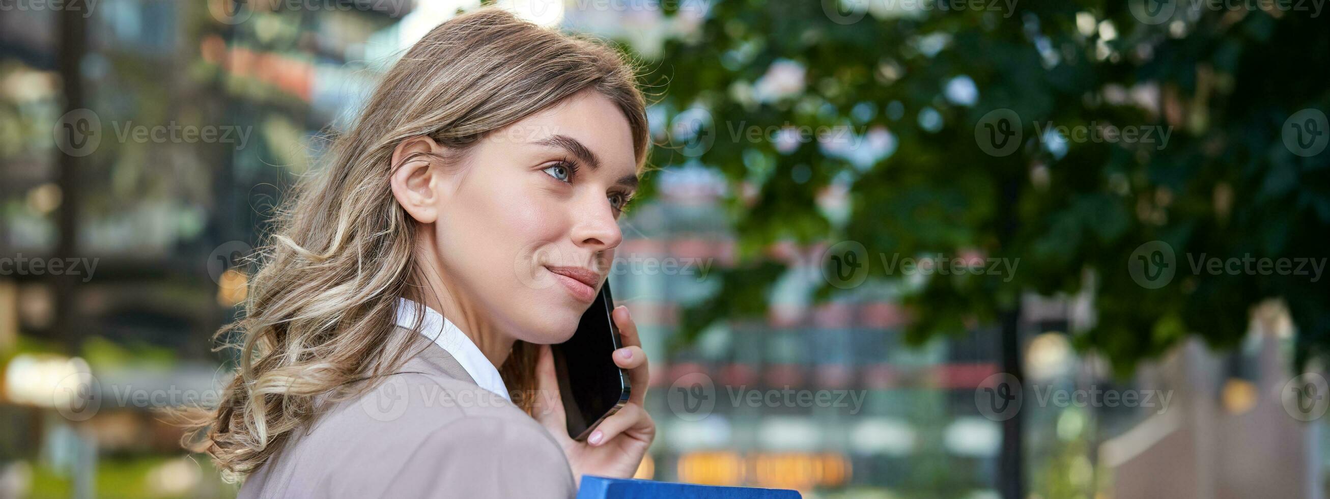 schließen oben Porträt von korporativ Frau Berufung auf Handy, Mobiltelefon Telefon, Gehen auf Straße mit Arbeit Unterlagen im Hand, tragen Geschäft passen foto