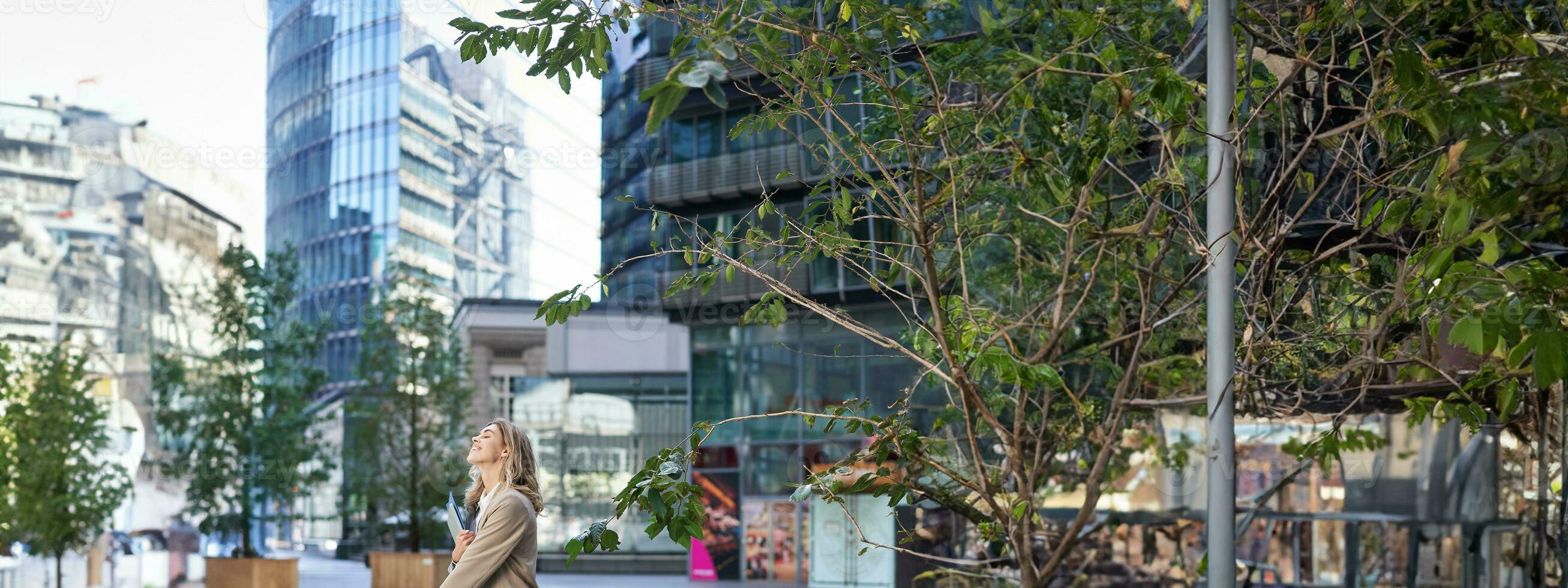 Vertikale Schuss von korporativ Frau im Beige passen Stehen draußen auf Straße, Getränke Morgen Kaffee wegbringen Vor Arbeit foto