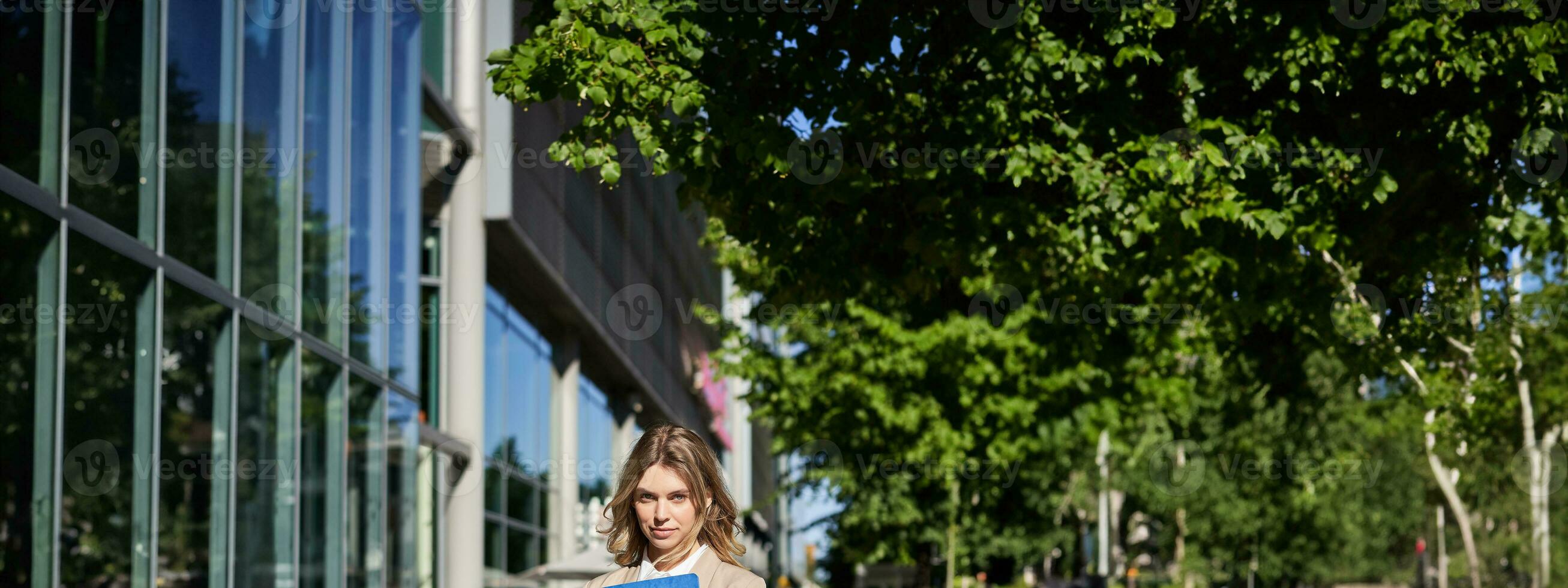 Vertikale Schuss von Geschäftsfrau mit Ordner, Stehen auf ein Straße in der Nähe von Büro Gebäude, tragen passen zum Büro Arbeit foto